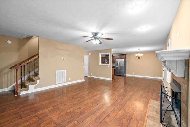 unfurnished living room with a tiled fireplace, ceiling fan with notable chandelier, hardwood / wood-style floors, and a textured ceiling