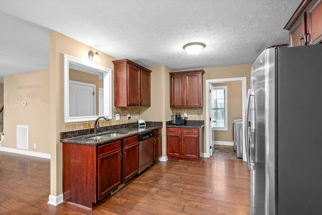 kitchen featuring sink, tasteful backsplash, appliances with stainless steel finishes, dark hardwood / wood-style flooring, and dark stone counters