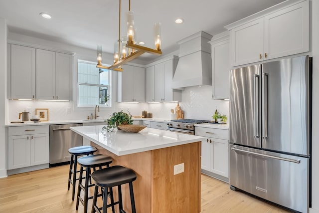 kitchen with custom exhaust hood, premium appliances, a kitchen island, pendant lighting, and white cabinets