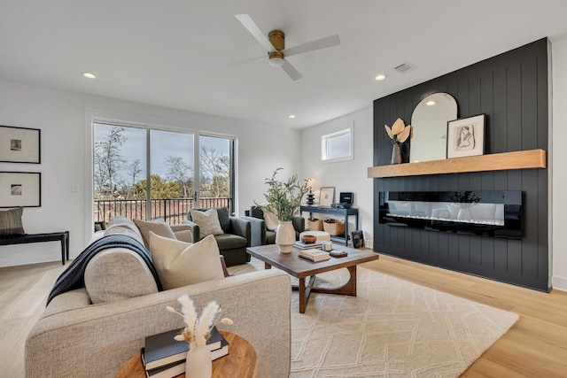 living room featuring ceiling fan, a large fireplace, and light hardwood / wood-style floors