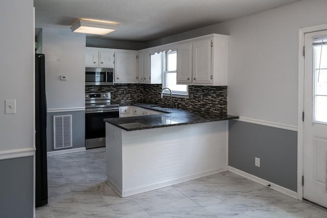 kitchen with sink, kitchen peninsula, white cabinets, stainless steel appliances, and backsplash