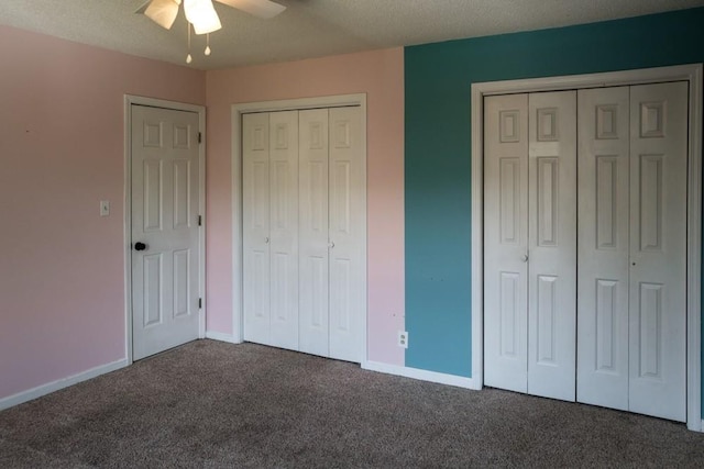 unfurnished bedroom featuring dark carpet, a textured ceiling, ceiling fan, and two closets