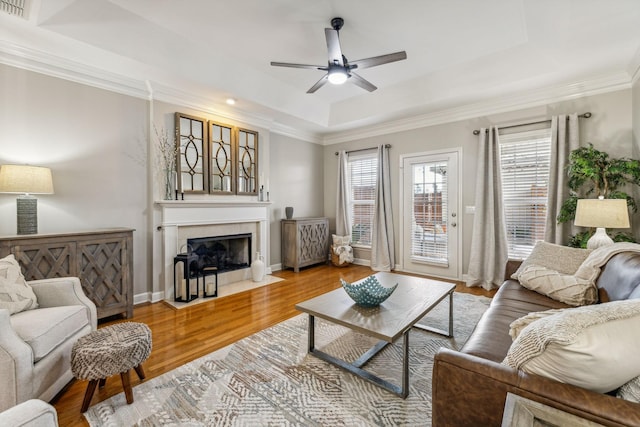 living room with a tray ceiling, ornamental molding, ceiling fan, and light wood-type flooring