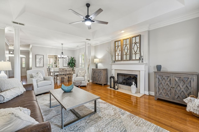 living room featuring ceiling fan with notable chandelier, a tray ceiling, hardwood / wood-style floors, and ornate columns