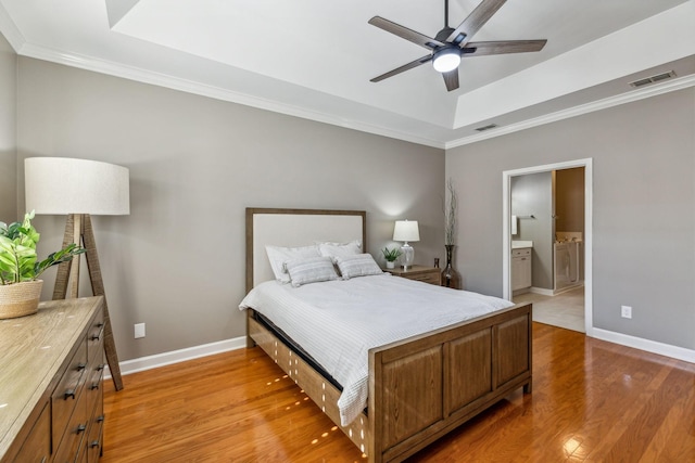 bedroom with ornamental molding, ceiling fan, light hardwood / wood-style floors, a raised ceiling, and ensuite bath