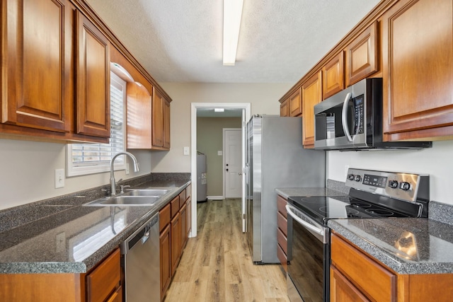 kitchen with appliances with stainless steel finishes, washer / clothes dryer, sink, light hardwood / wood-style floors, and a textured ceiling