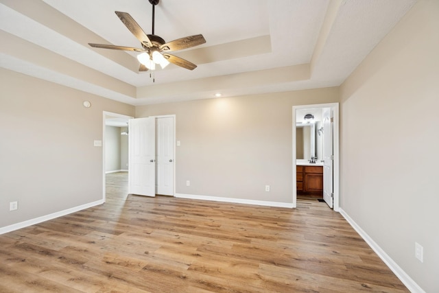 unfurnished bedroom with ensuite bathroom, a tray ceiling, and light hardwood / wood-style floors