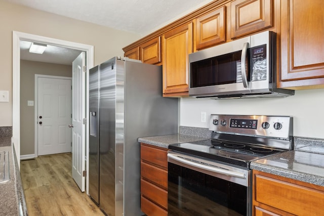 kitchen with light wood-type flooring, dark stone counters, and appliances with stainless steel finishes