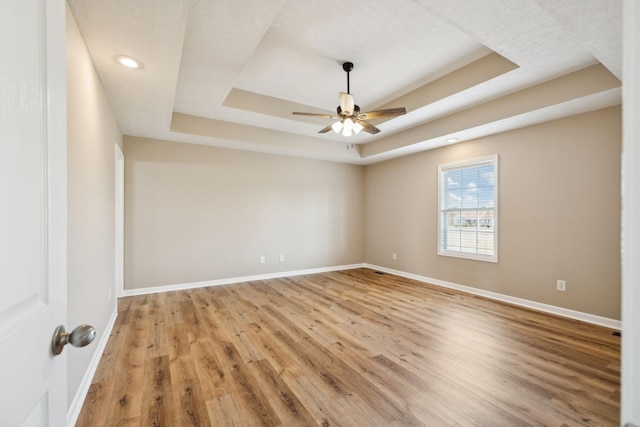 unfurnished room featuring light hardwood / wood-style flooring, ceiling fan, and a tray ceiling