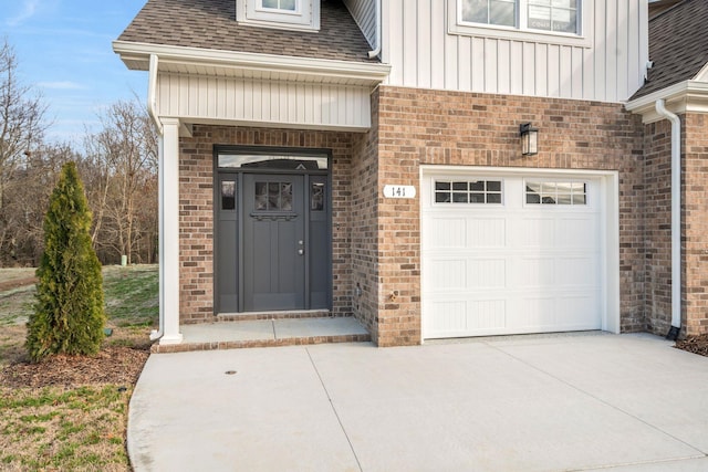 property entrance with board and batten siding, roof with shingles, brick siding, and a garage