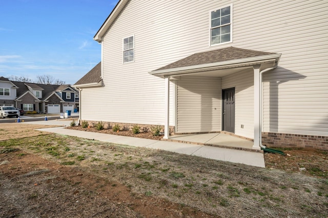 doorway to property featuring a patio, a shingled roof, and a residential view