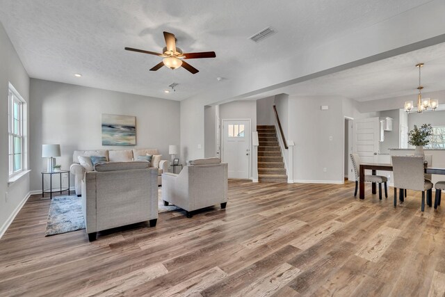 living area featuring a textured ceiling, wood finished floors, visible vents, baseboards, and stairway