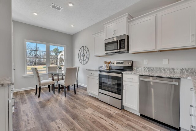 kitchen with stainless steel appliances, white cabinets, light wood-style floors, and visible vents