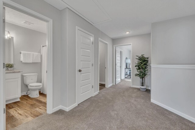 hallway featuring light carpet, visible vents, attic access, and baseboards