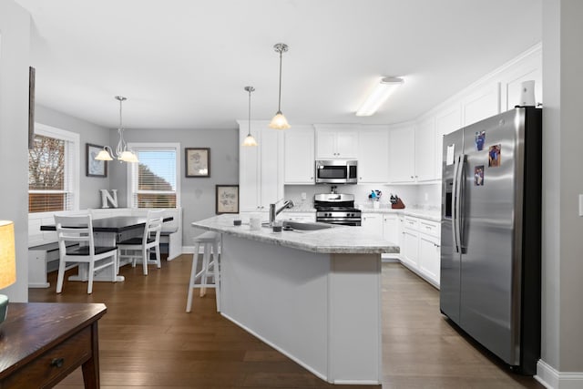 kitchen featuring appliances with stainless steel finishes, pendant lighting, white cabinetry, an island with sink, and sink