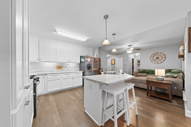 kitchen with appliances with stainless steel finishes, white cabinets, hanging light fixtures, hardwood / wood-style flooring, and a center island with sink