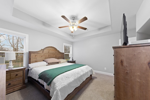 bedroom featuring ceiling fan, a tray ceiling, light carpet, and multiple windows