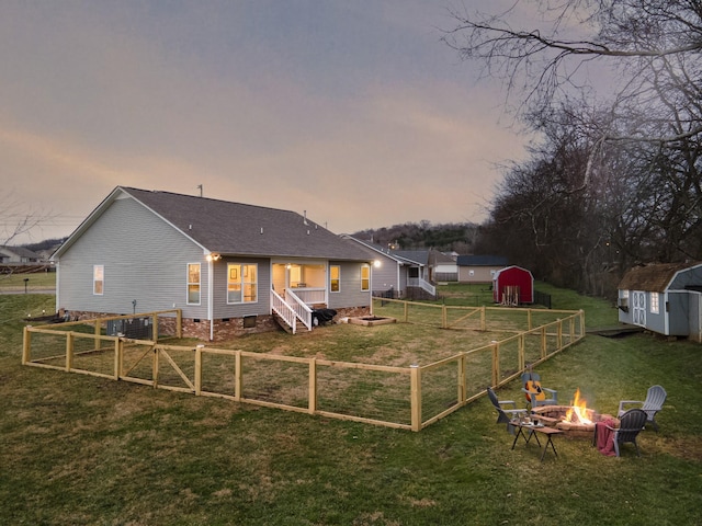 back house at dusk featuring a storage unit, a lawn, and a fire pit