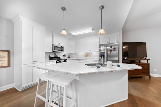 kitchen with white cabinetry, stainless steel appliances, decorative light fixtures, and a kitchen island with sink