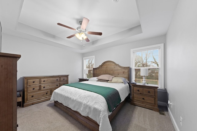 bedroom with ceiling fan, a tray ceiling, and light carpet