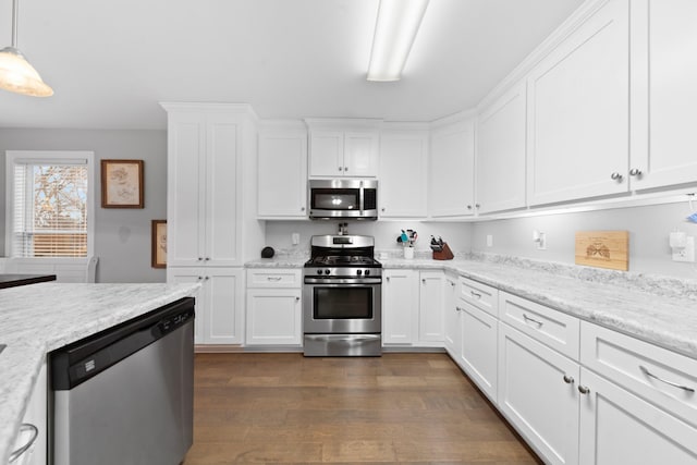 kitchen featuring dark wood-type flooring, stainless steel appliances, light stone countertops, white cabinets, and decorative light fixtures