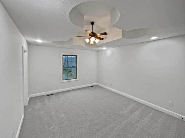 carpeted empty room featuring a textured ceiling, a raised ceiling, and ceiling fan