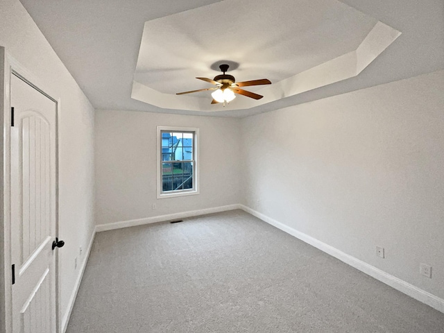 empty room featuring a raised ceiling, ceiling fan, and carpet