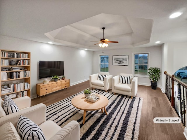 living room with a tray ceiling, dark hardwood / wood-style floors, and ceiling fan