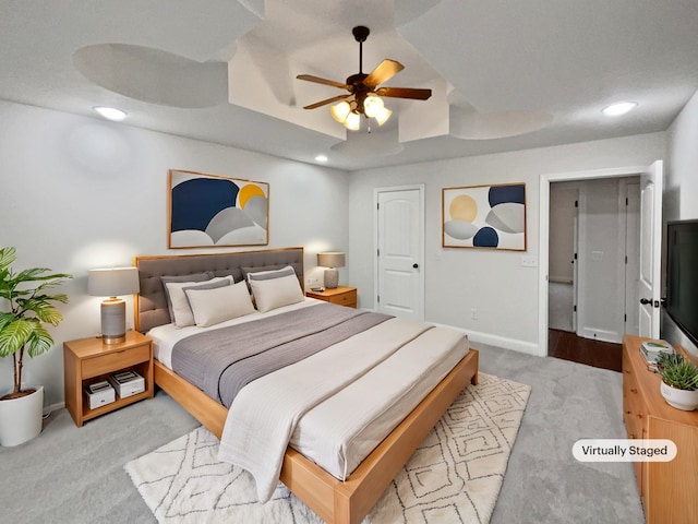 bedroom with light carpet, ceiling fan, and a tray ceiling