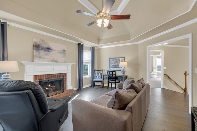 living room featuring a brick fireplace, ornamental molding, a tray ceiling, ceiling fan, and hardwood / wood-style floors