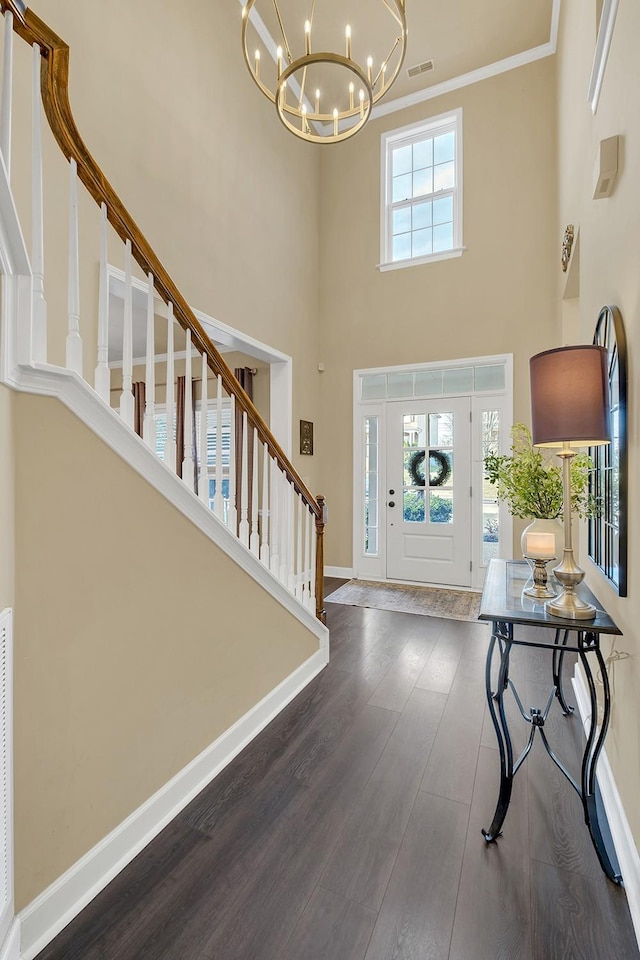 entrance foyer with a towering ceiling, ornamental molding, dark hardwood / wood-style floors, and a notable chandelier