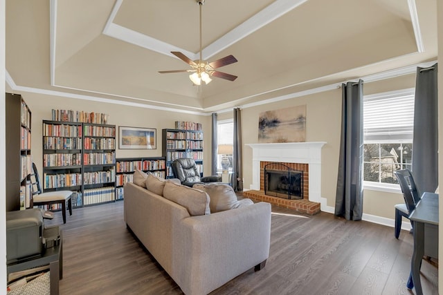 living room featuring dark hardwood / wood-style floors, plenty of natural light, a tray ceiling, and a brick fireplace