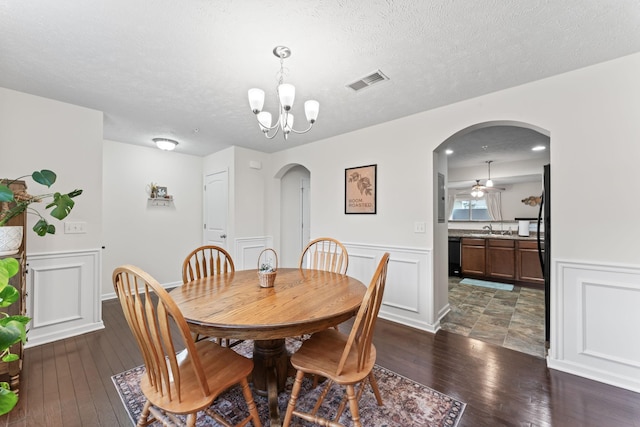 dining space featuring dark wood-type flooring, sink, ceiling fan with notable chandelier, and a textured ceiling