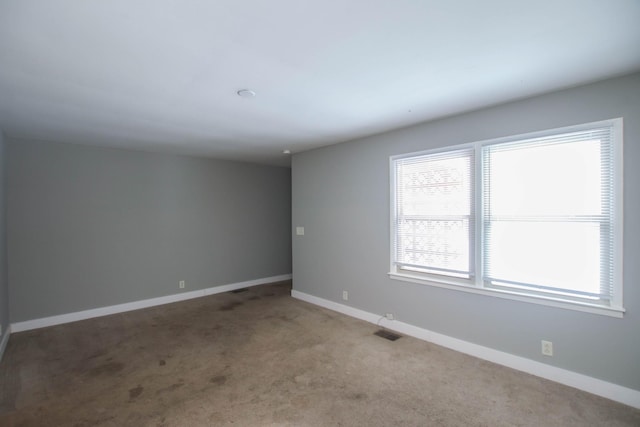 empty room with carpet floors, visible vents, and baseboards