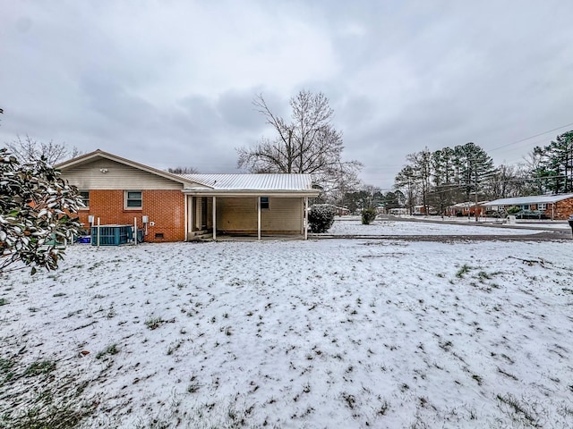 snow covered rear of property with cooling unit and brick siding