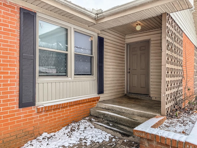 snow covered property entrance featuring brick siding