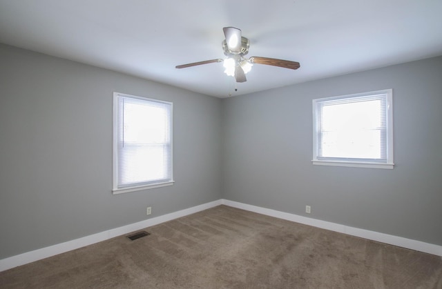 carpeted spare room featuring a healthy amount of sunlight, visible vents, ceiling fan, and baseboards