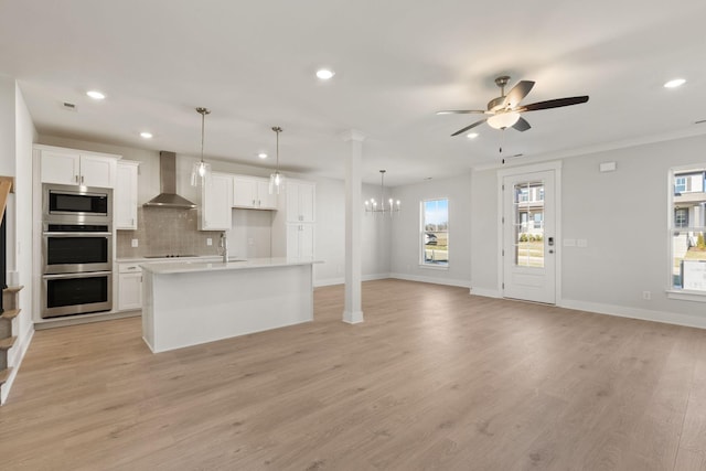 kitchen featuring hanging light fixtures, a center island with sink, appliances with stainless steel finishes, wall chimney range hood, and white cabinets