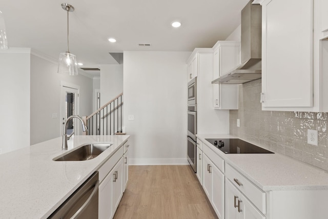 kitchen featuring wall chimney range hood, sink, appliances with stainless steel finishes, white cabinetry, and light stone counters