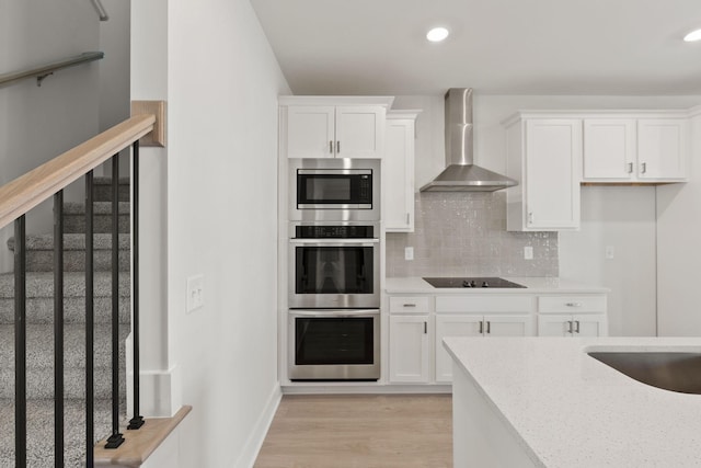 kitchen with tasteful backsplash, white cabinetry, light hardwood / wood-style floors, stainless steel appliances, and wall chimney range hood