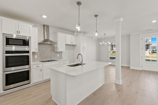 kitchen with wall chimney exhaust hood, sink, white cabinetry, appliances with stainless steel finishes, and a kitchen island with sink