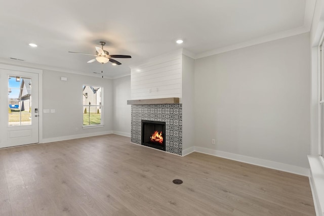 unfurnished living room featuring crown molding, ceiling fan, a tiled fireplace, and light hardwood / wood-style flooring