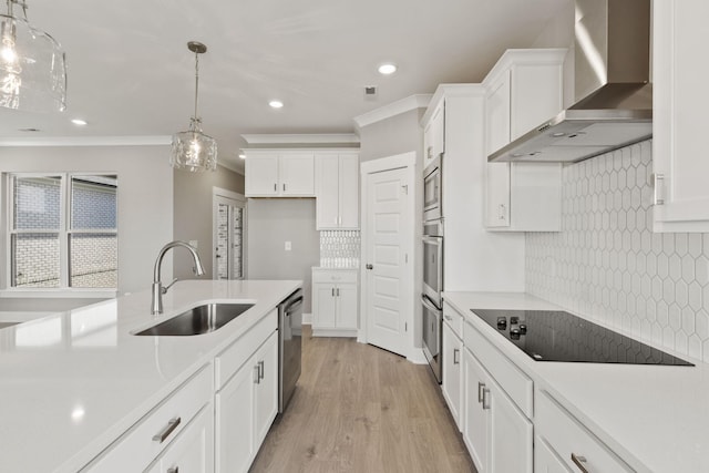 kitchen with appliances with stainless steel finishes, pendant lighting, sink, white cabinets, and wall chimney range hood