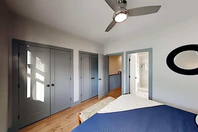 bedroom featuring two closets, light hardwood / wood-style flooring, ensuite bath, and ceiling fan