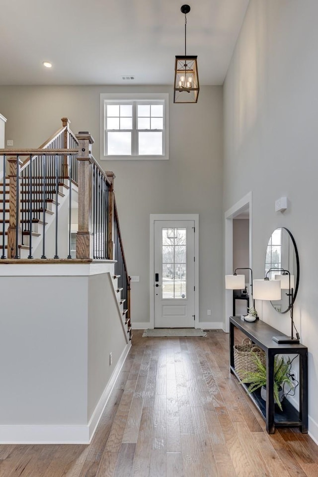 entryway with plenty of natural light, a towering ceiling, a chandelier, and light hardwood / wood-style floors