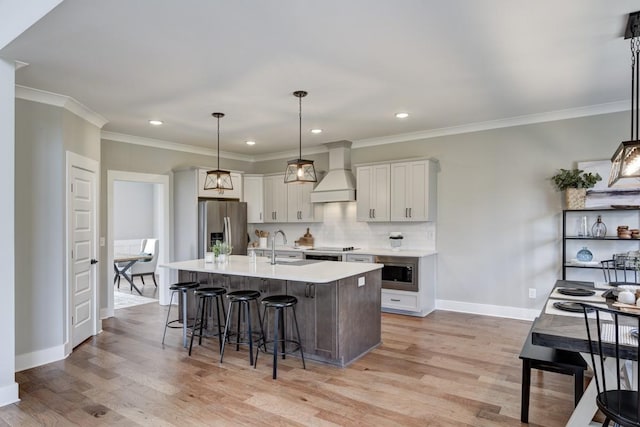 kitchen with appliances with stainless steel finishes, white cabinets, a center island with sink, decorative light fixtures, and custom exhaust hood