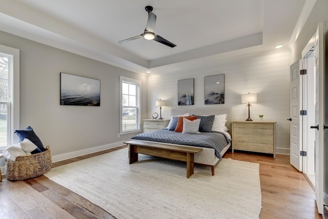 bedroom with ceiling fan, a tray ceiling, and light wood-type flooring