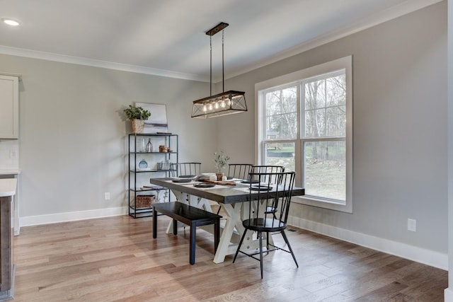 dining space with ornamental molding and light hardwood / wood-style flooring