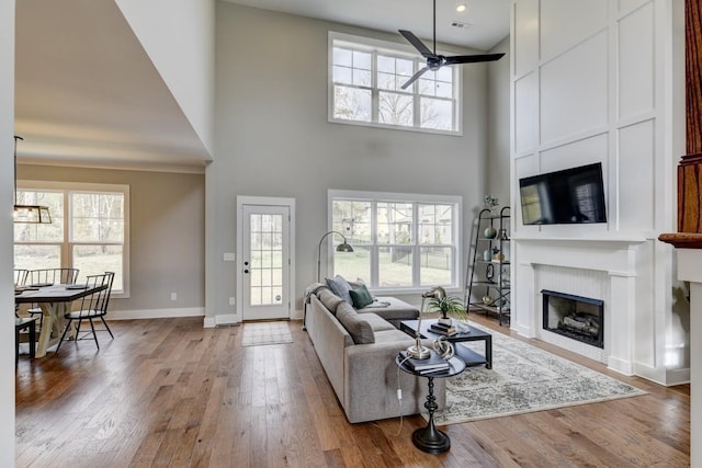 living room with hardwood / wood-style flooring, ceiling fan, a high ceiling, and a fireplace