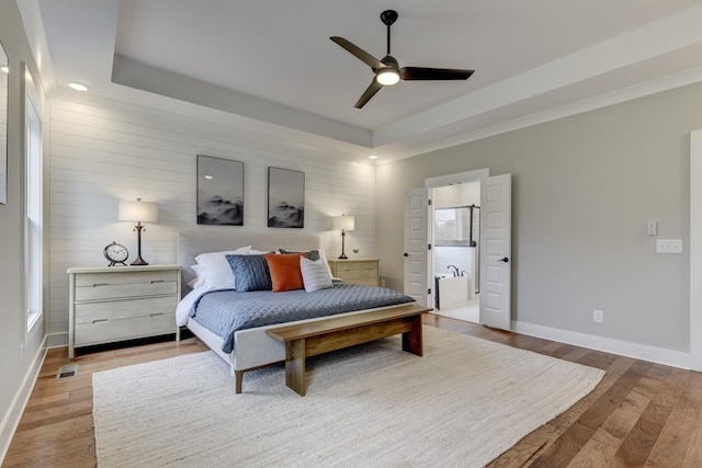 bedroom with a raised ceiling, ceiling fan, and light wood-type flooring